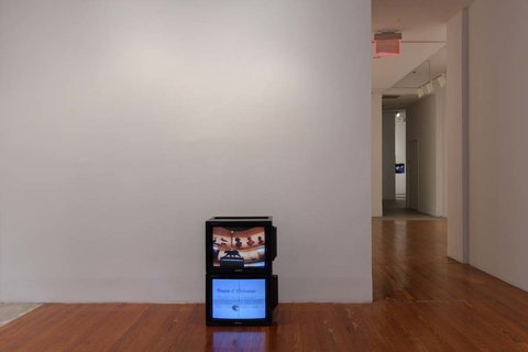 Installation view of the exhibition featuring two television monitors stacked on top of one another. 