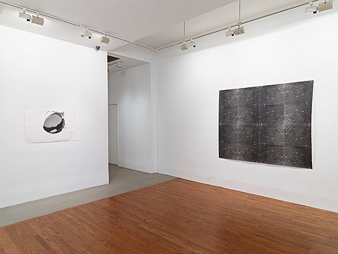 Two black and white images hang on a gallery's walls. One is comprised of a 4x4 grid of black sheets with white dots.