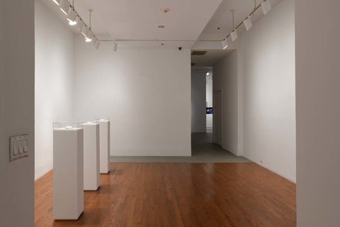 Installation image of the exhibition featuring three white pedestals on the left side of the frame. 