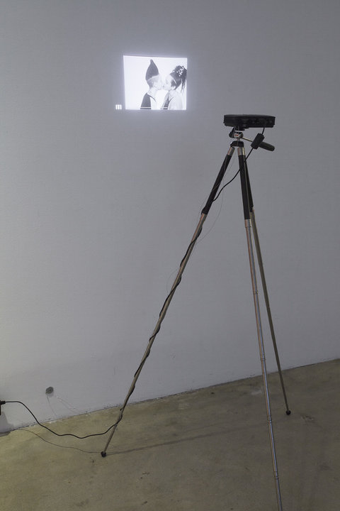 A projector displaying a small projection of two women kissing on the wall in black and white. 