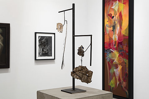 A sculpture on a wire hanger is dispayed in front of several framed wall artworks.