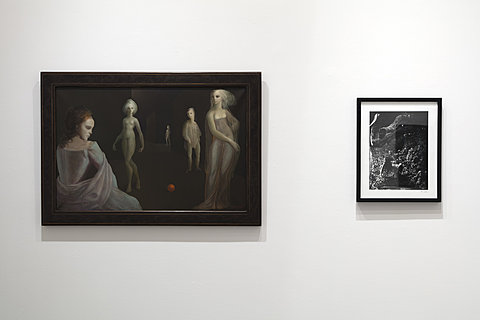 Two hanging artworks, one a painting of wraith-like figures, and one a black-and-white photograph.