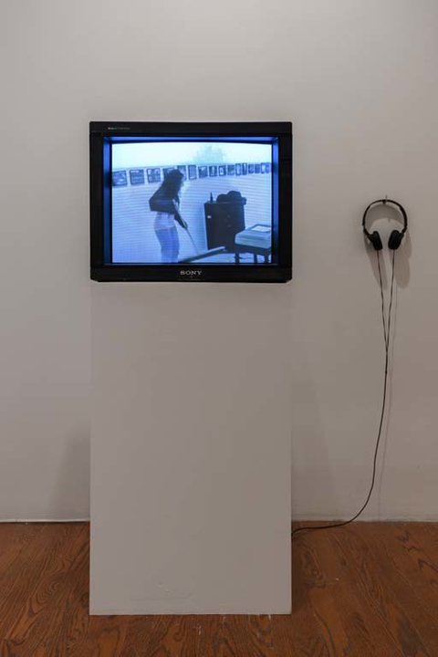 Installation image of a white pedestal featuring a television monitor sitting on top of it. 