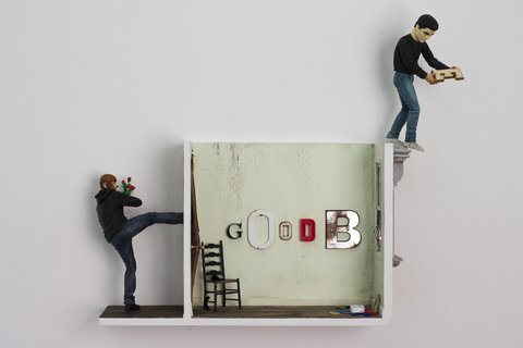 Image of a sculpture from the exhibition featuring a fake green, model sized room. The letters G, O, O, D, B, and Y are on the wall. the letter Y holds up the window. A figure on the left, outside of the room lifts up his leg to kick the wall. On the right, another figure braces to jump from the top edge of the wall. 