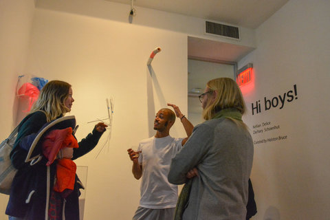 Installation image of visitors visiting the exhibition featuring figures engaging in conversation in the gallery. 