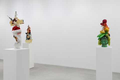 Installation view of three white pedestals with sculptures scattered across the room.  