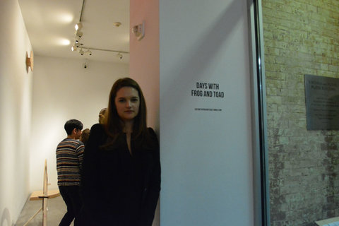 Image of a person standing next to the wall text featuring the title of the exhibition. The text states, "DAYS WITH FROG AND TOAD." The figure is in partial shadow and blocks most of the doorway from the viewers view. 
