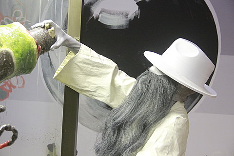 The side profile of a person wearing white is lifting their left arm. They have long grey hair completely covering their face. A white brimmed hat covers their face and head.