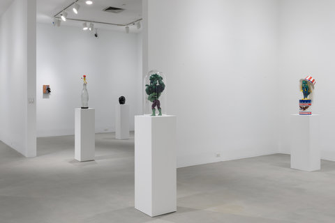 Installation view of four white pedestals with sculptures atop them scattered throughout the rooms. 