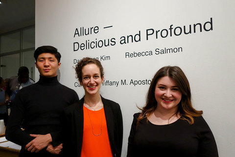 Image of visitors standing in front of vinyl wall text at the exhibition. The wall text says, "ALLURE-- DELICIOUS AND PROFOUND, DAE YOUNG KIM, REBECCA SALMON, CURATED BY TIFFANY M. APOSTOLOU."