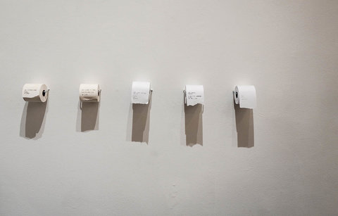 Image from the exhibition featuring five toilet paper rolls hanging against a white wall. 