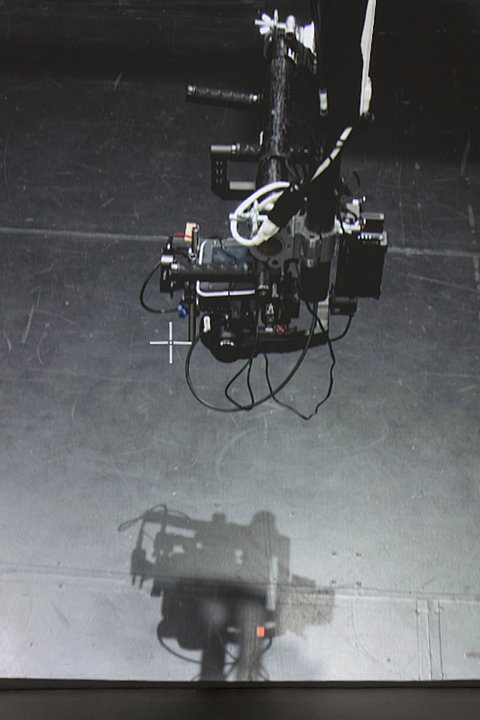 A close up of a a camera on a moving rig mounted directly in front of a large projection. The camera is focusing on a small white cross.