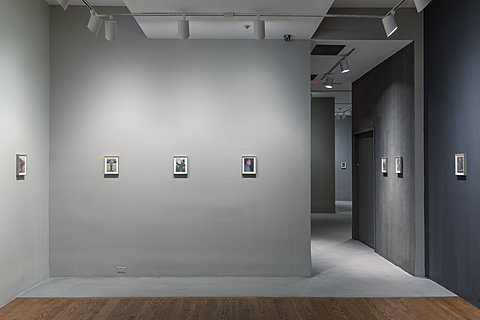 A gallery with gray walls and numerous small pictures of Chairman Mao mounted on the wall.
