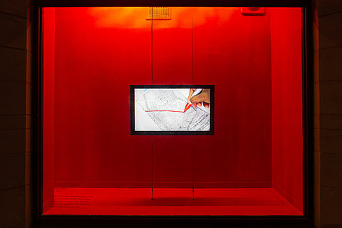 A television monitor displaying a red pen crossing out text on a piece of paper hangs against a red background.